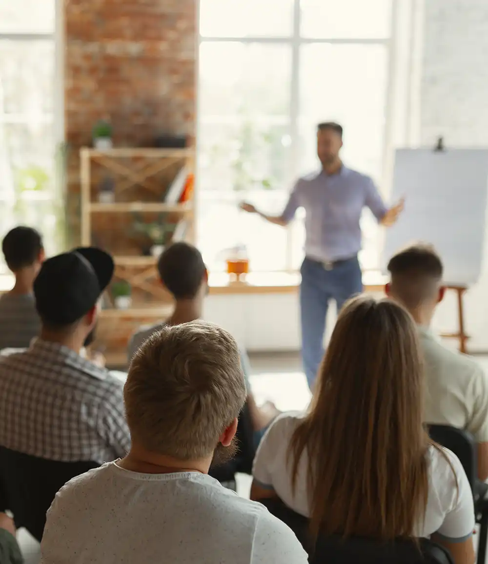 Männlicher Redner hält Vortrag in einem Saal bei einem Universitätsworkshop. Publikum oder Konferenzsaal. Rückansicht von nicht erkennbaren Teilnehmern im Publikum. 
